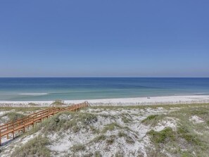 Une plage avec une promenade en bois menant au rivage, des dunes de sable et un ciel bleu dégagé.