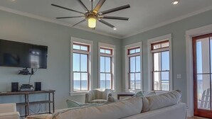 A spacious living room with a large white sofa, a ceiling fan, and a flat-screen TV mounted on the wall. - Sea Section (Port St. Joe)