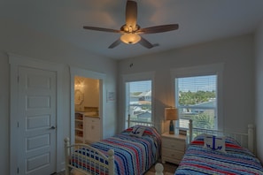A bedroom with two beds, a ceiling fan, a window with blinds, and a view of the outside. - Mermaid Kisses (Port St. Joe)