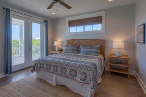 Ein Schlafzimmer mit einem großen Bett, zwei Nachttischen inklusive Lampen, einem Deckenventilator, einem Fenster mit Jalousien und einem Balkon.