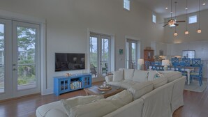 A spacious living room with a large sectional sofa, a blue entertainment unit, and a television. - Sunset Cottage (Port St. Joe)
