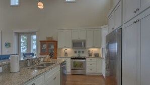 A modern kitchen with white cabinets, granite countertops, stainless steel appliances, and a wooden cabinet with glass doors. - Sunset Cottage (Port St. Joe)