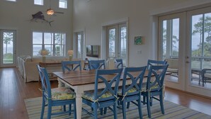 A spacious dining area with a wooden table and blue chairs, large windows, and a view of the outdoors. - Sunset Cottage (Port St. Joe)