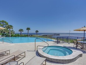 A pool area with a hot tub, lounge chairs, and umbrellas, overlooking a beach and ocean. - Cape Retreat (Port St. Joe)
