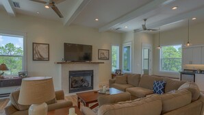 A spacious living room with a fireplace, a large sofa, a television, and a ceiling fan.