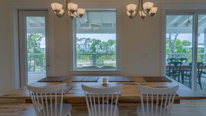 A dining area with a wooden table and white chairs, large windows with a view of trees and a balcony.