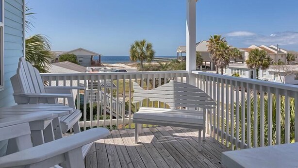 Une terrasse en bois, dotée de rampes et de chaises blanches, qui offre une vue sur une plage et des immeubles résidentiels.