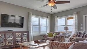 A spacious living room with a ceiling fan, large windows, a flat-screen TV, and a cozy seating area with a coffee table. - Shore to be Fun (Port St. Joe)
