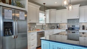 A modern kitchen with white cabinets, stainless steel appliances, a built-in oven, and a blue island. - Shore to be Fun (Port St. Joe)