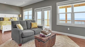 A spacious living room with a grey sofa, a coffee table, and a view of the ocean through large windows. - Shore to be Fun (Port St. Joe)