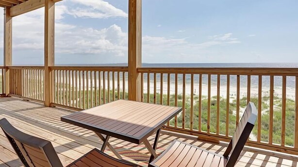 A wooden deck with a table and chairs, overlooking a beach. - Shore to be Fun (Port St. Joe)