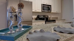 A kitchen with white cabinets, a microwave, an oven, and a decorative metal sculpture. - 4 Better Vues (Port St. Joe)