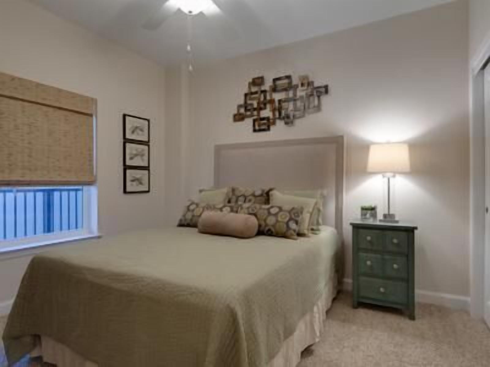 A bedroom with a bed, a nightstand, a wall-mounted lamp, and a window with blinds.