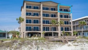 Un hotel de varios pisos con balcones en cada planta, situado cerca de una playa de arena y palmeras.