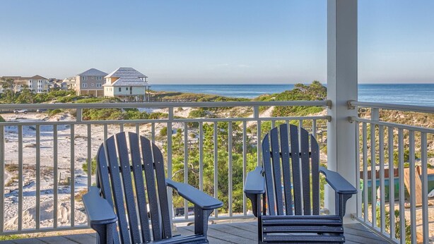 A balcony with two Adirondack chairs overlooking a beach with houses in the background. - Maui Escape (Port St. Joe)