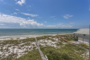 A beach view with a wooden walkway leading to a building with a metal roof.