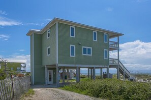 A two-story beachfront house with a covered porch and a staircase leading to a balcony.