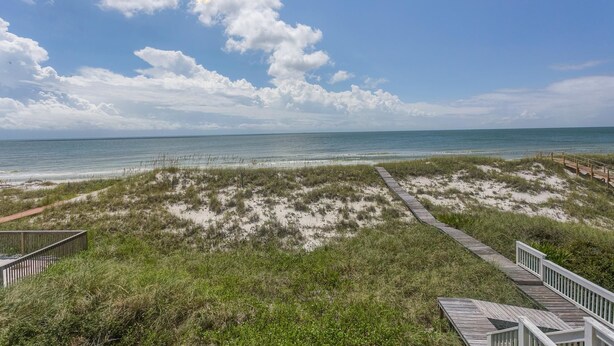 A beach with a wooden boardwalk leading to the shore, surrounded by grassy dunes. - Serenity Now (Port St. Joe)