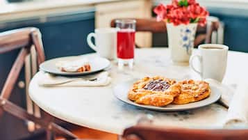 Una mesa de desayuno con pasteles, una taza de café y un vaso de bebida roja.