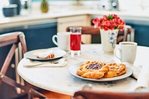 A breakfast table with pastries, a cup of coffee, and a glass of red beverage.