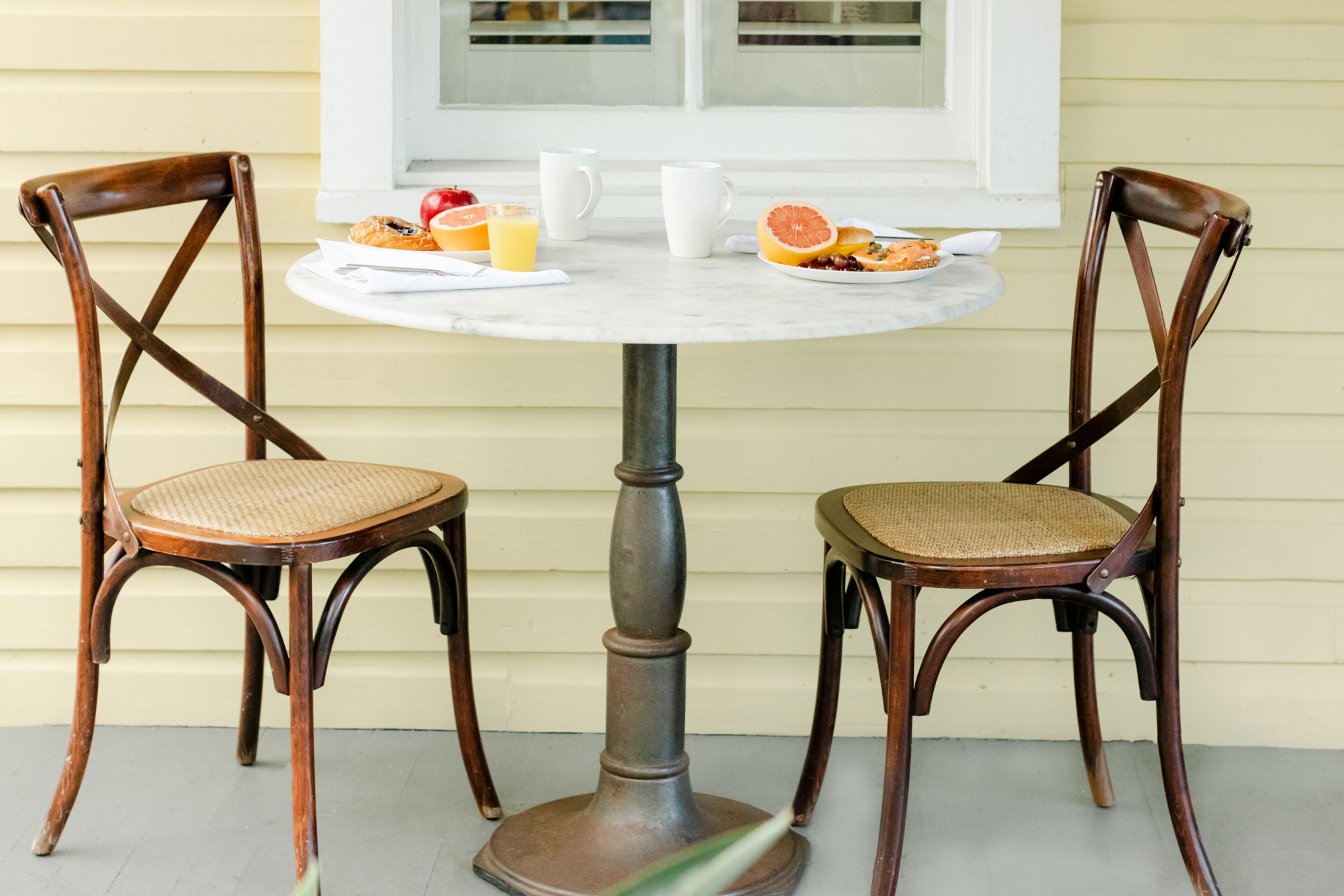 A round table with two wooden chairs, a white pitcher, and a plate with food and drinks.