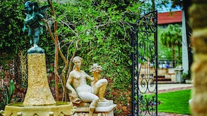 A garden with a statue of a seated figure, a fountain, and a wrought iron gate.