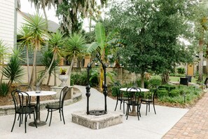 An outdoor patio with round tables and chairs, surrounded by lush greenery and a stone wall. - The Collector Inn - Adults Only (St. Augustine)