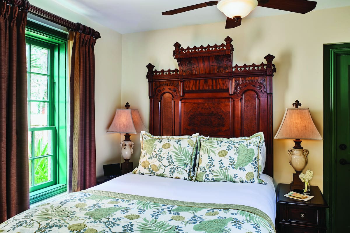 A bedroom with a large bed, two bedside lamps, a wooden headboard, and a green window.