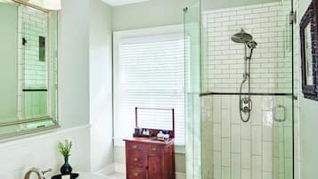 Une salle de bain équipée d’un meuble-lavabo, d’un miroir, d’une douche avec une porte en verre et d’une fenêtre avec des stores.