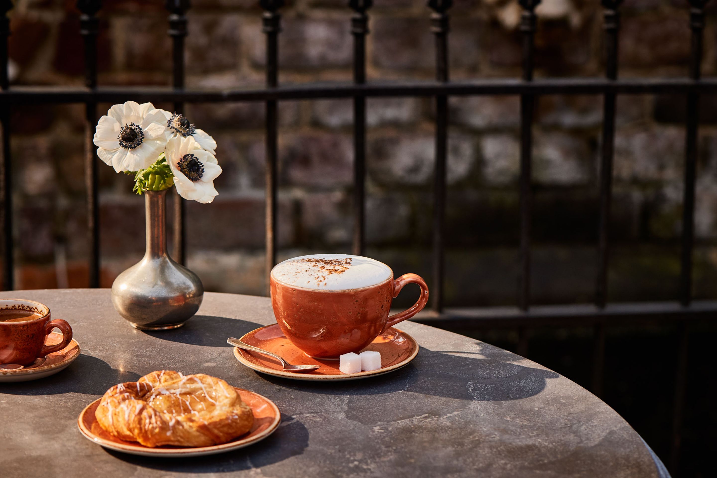 A table with a coffee cup, a pastry, and a vase with flowers.