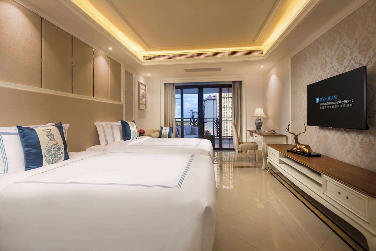 Habitación de hotel con dos camas, televisión, escritorio y vista a la ciudad.
