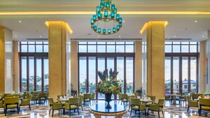 A spacious lobby with a large chandelier, a central table with a vase of flowers, and a view of the outdoors through large windows. - Wyndham Hainan Clearwater Bay Resort (Lingshui)