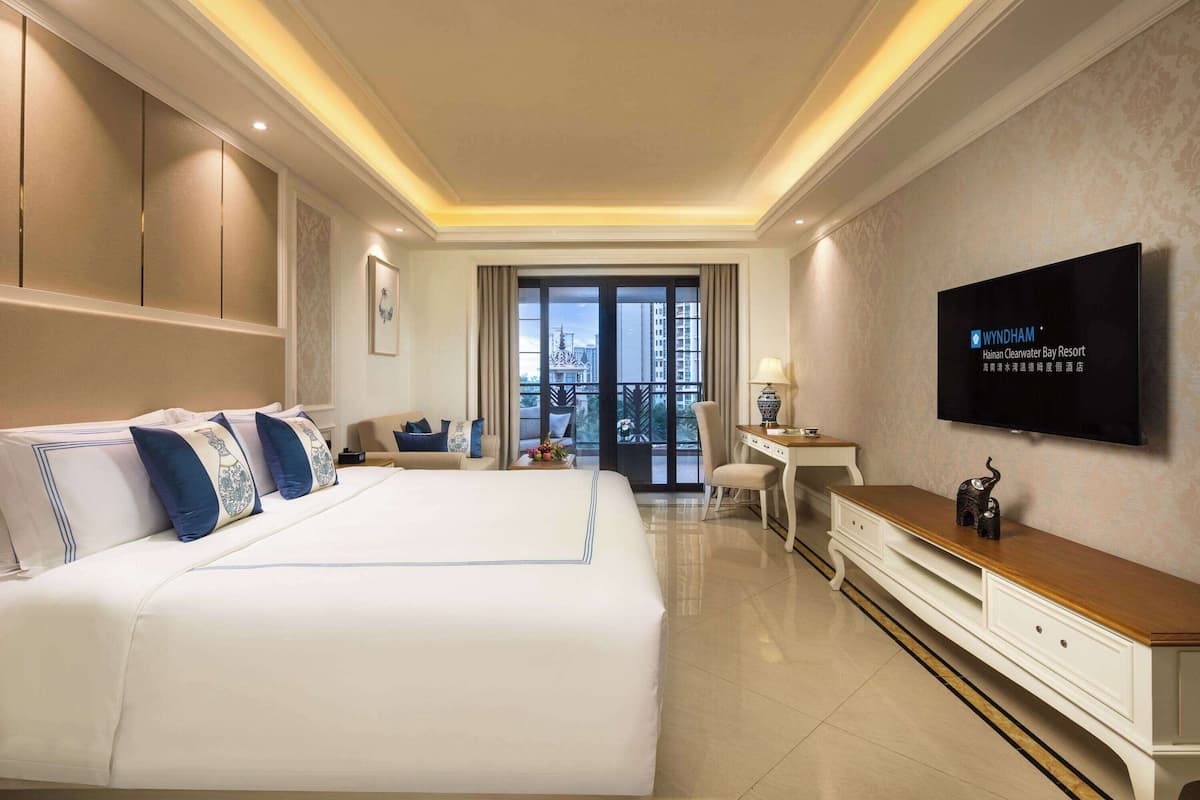 Habitación de hotel con una cama grande, un escritorio, televisión y vistas a la ciudad.
