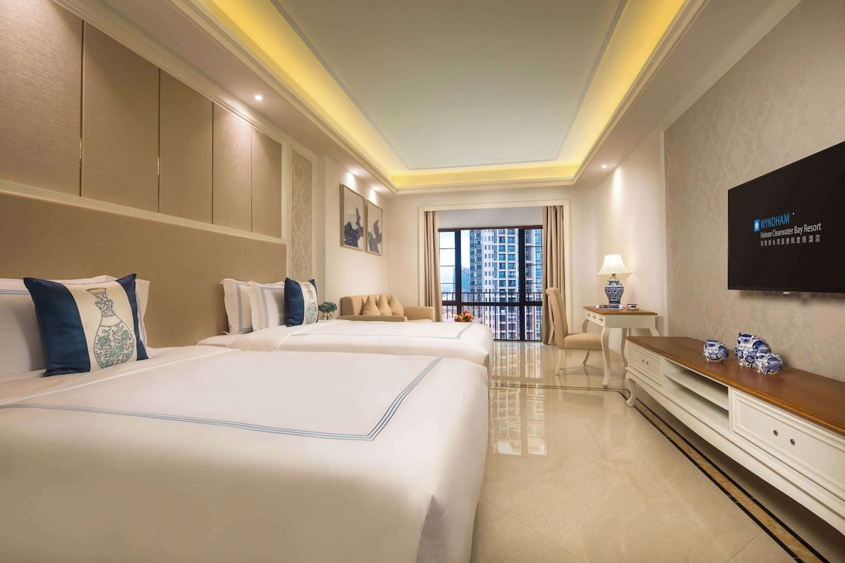 Habitación de hotel con dos camas, televisión, escritorio y vista a la ciudad.