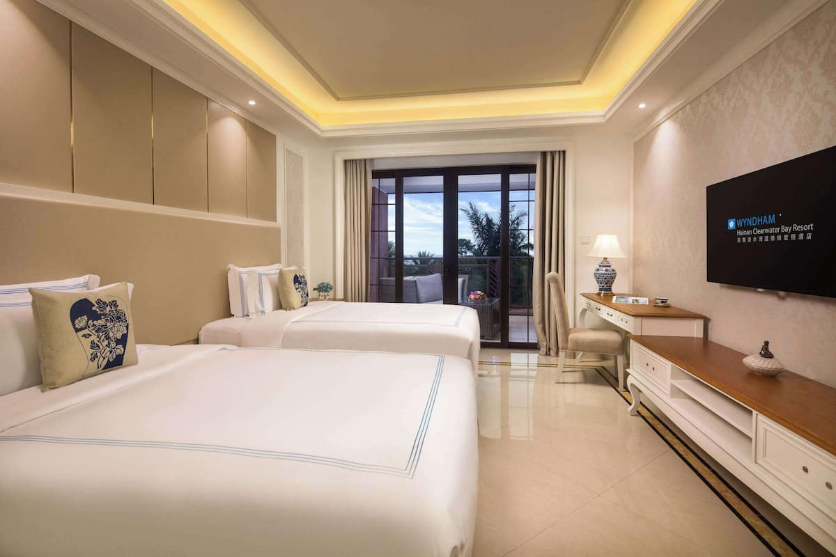 Habitación de hotel con dos camas, televisión, escritorio y vistas al exterior.