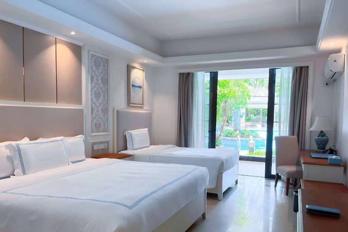 Habitación de hotel con dos camas, un escritorio, una silla y un ventanal con vistas a zonas verdes.
