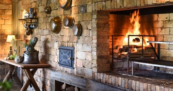 Una chimenea de ladrillo rústica con fuego, rodeada de estantes con utensilios de cocina y un banco de madera.