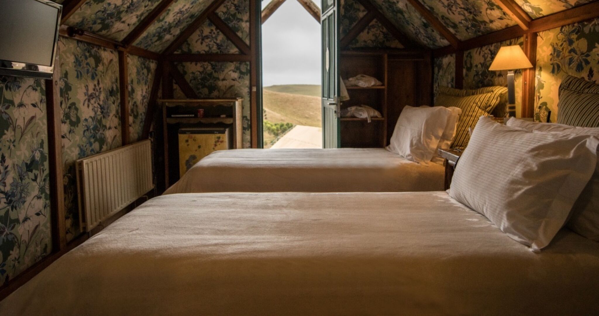 Un dormitorio con dos camas, techo de madera, radiador, televisión y vistas al campo.