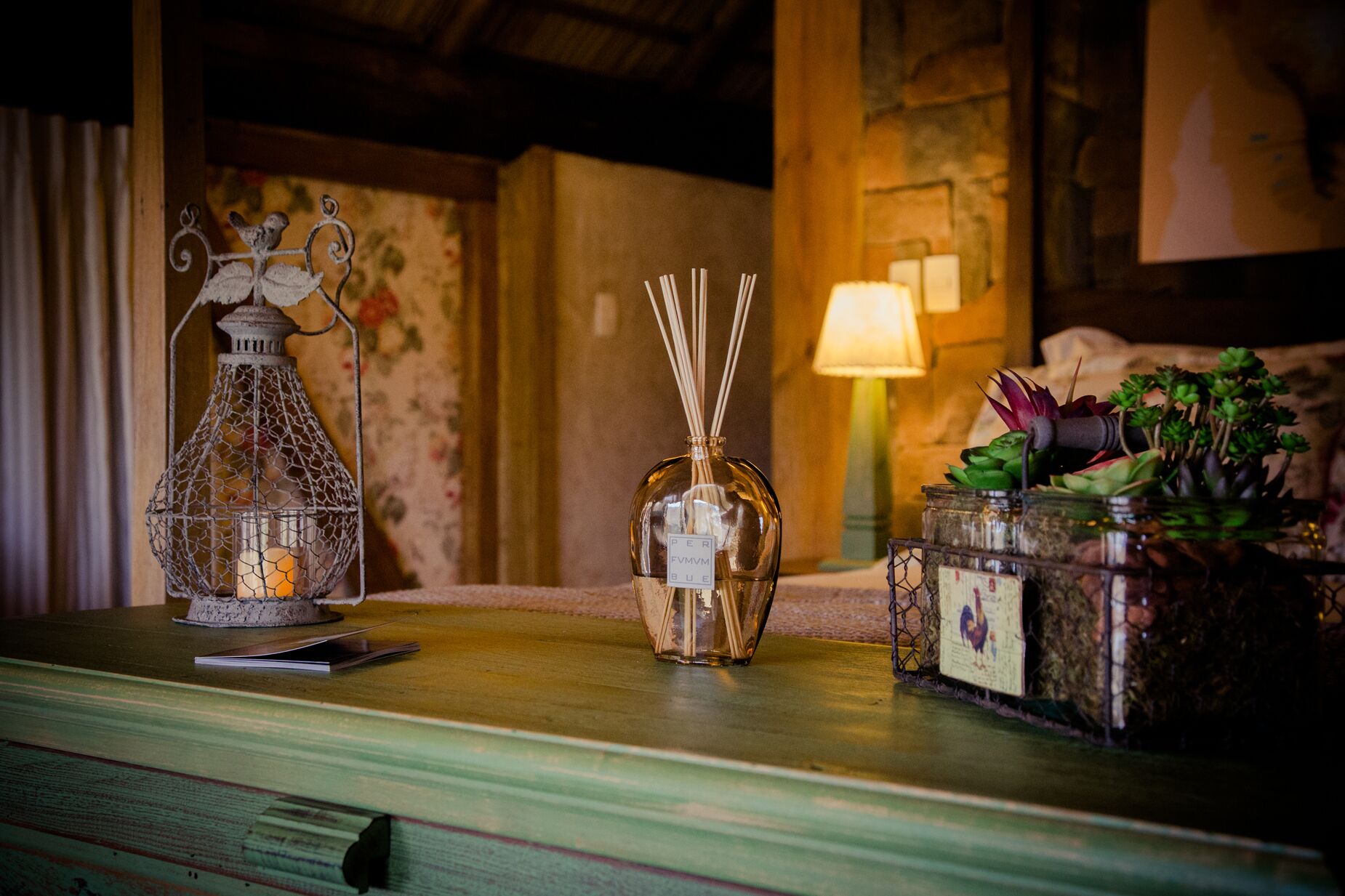 A wooden table with a decorative metal lantern, a glass bottle with reed sticks, and a small terrarium with succulents.