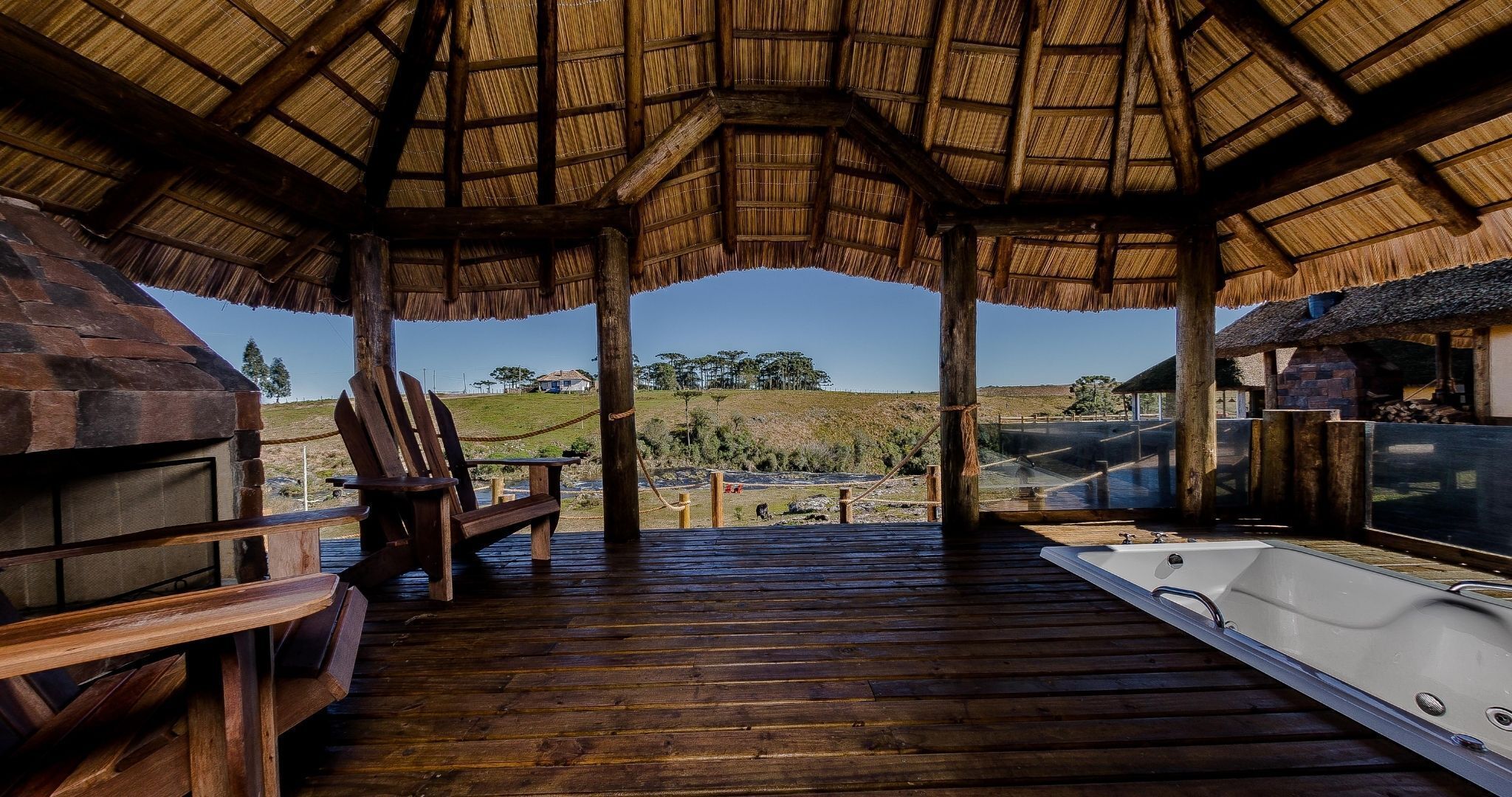 Een houten terras met een jacuzzi, houten stoelen en een rieten dakconstructie.