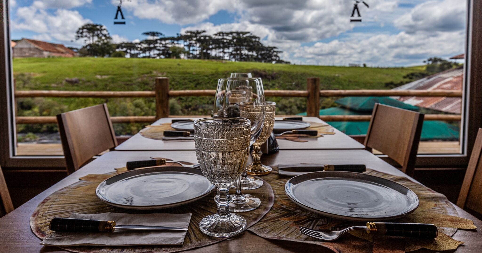 A dining table set with plates, glasses, and cutlery, overlooking a scenic landscape.