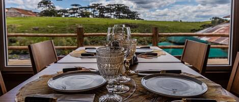 A dining table set with plates, glasses, and cutlery, overlooking a scenic landscape.