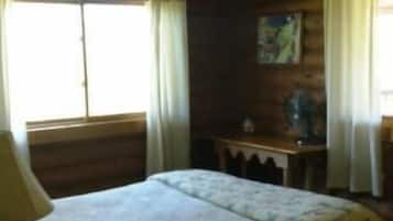 Um quarto com cama, escrivaninha e janela com cortinas.
