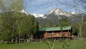 A wooden cabin with a green roof, surrounded by a wooden fence, set against a backdrop of snow-capped mountains and trees. - Star Mesa 2 Bedroom Holiday Home By Pinon Vacation Rentals (Howard)