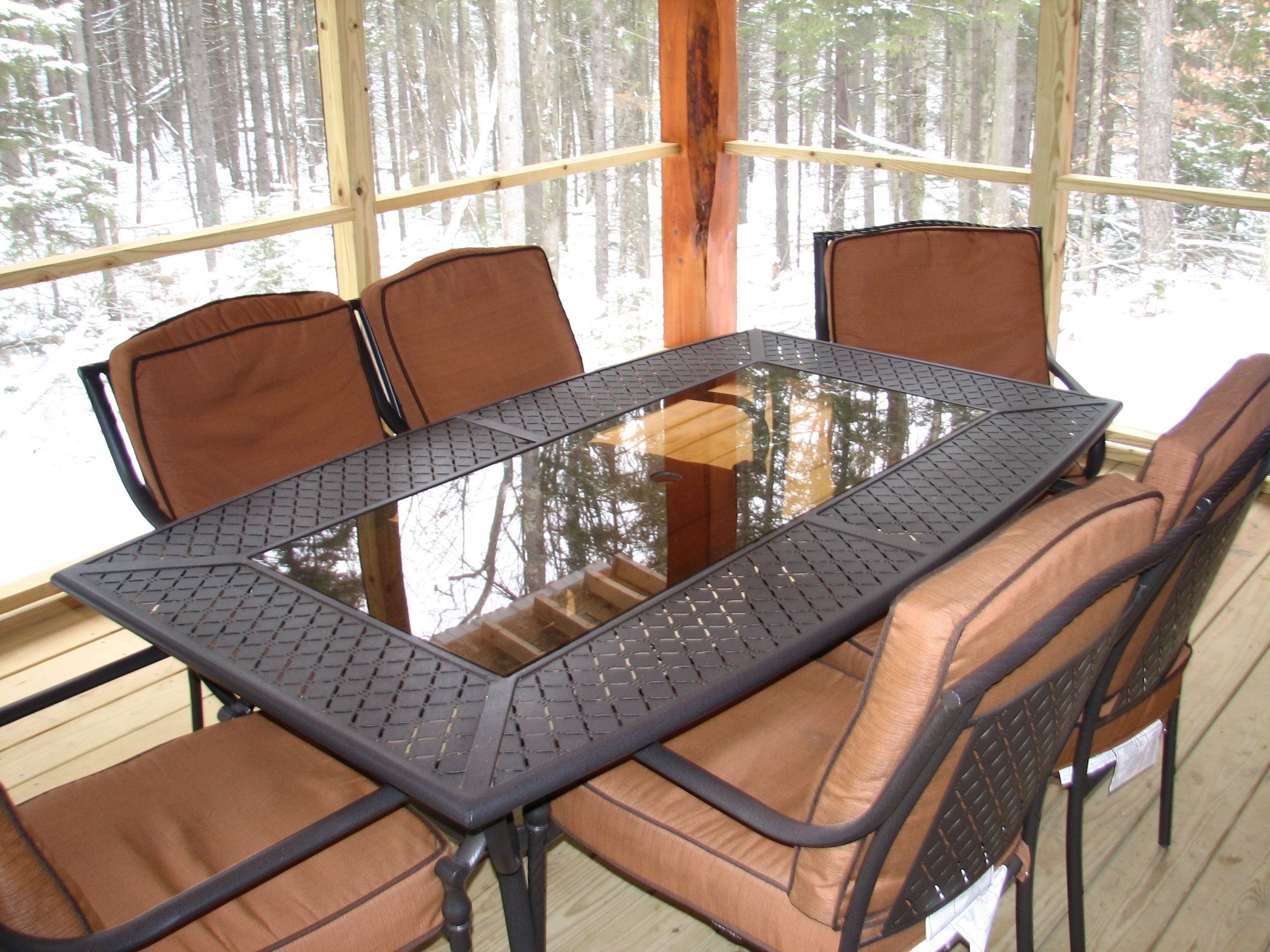 A glass-top table with metal frame and cushioned chairs in a room with large windows.