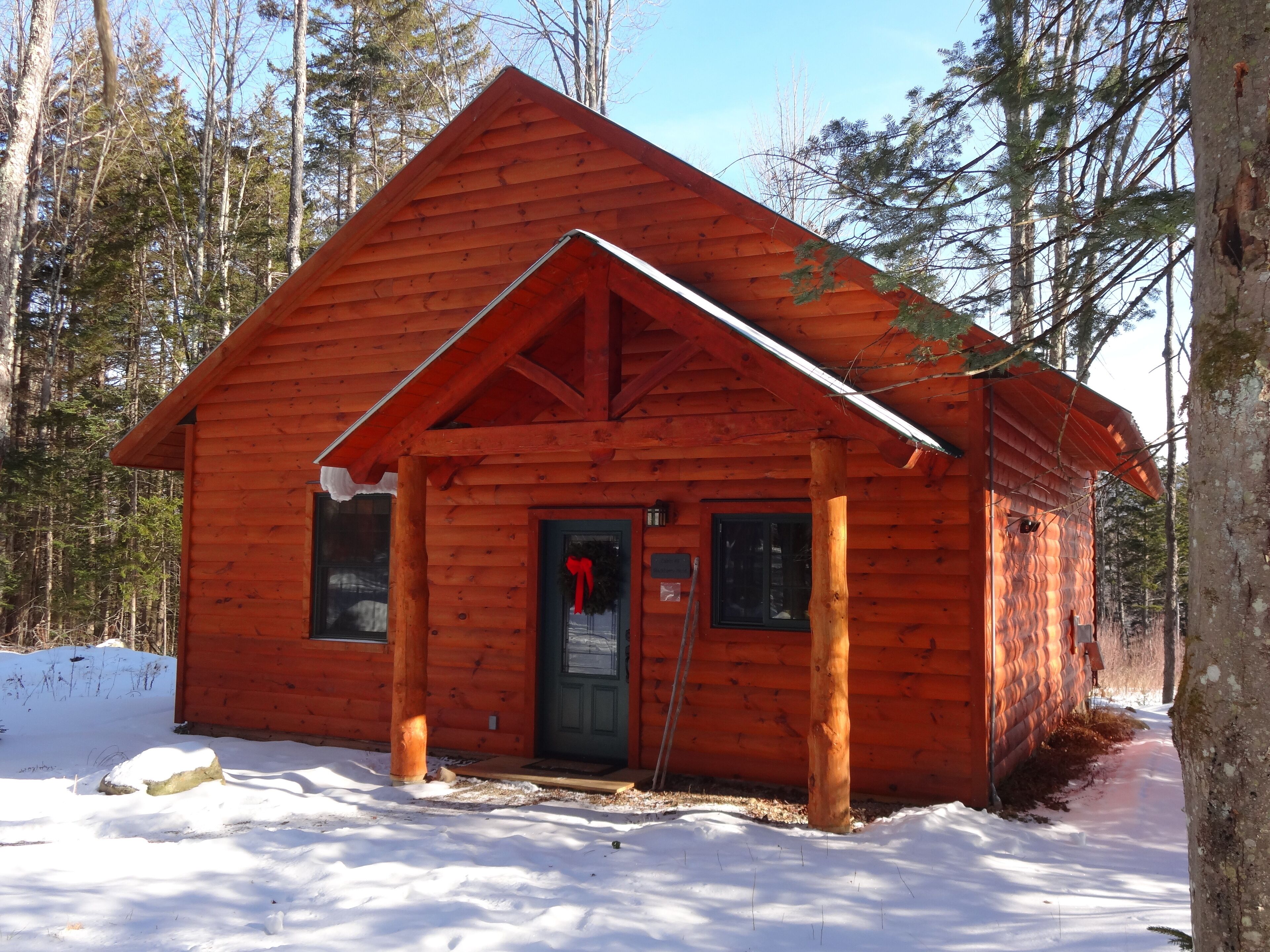 Une petite cabane en bois, d’un seul étage, avec un toit à pignon, une porte d’entrée et un petit porche.