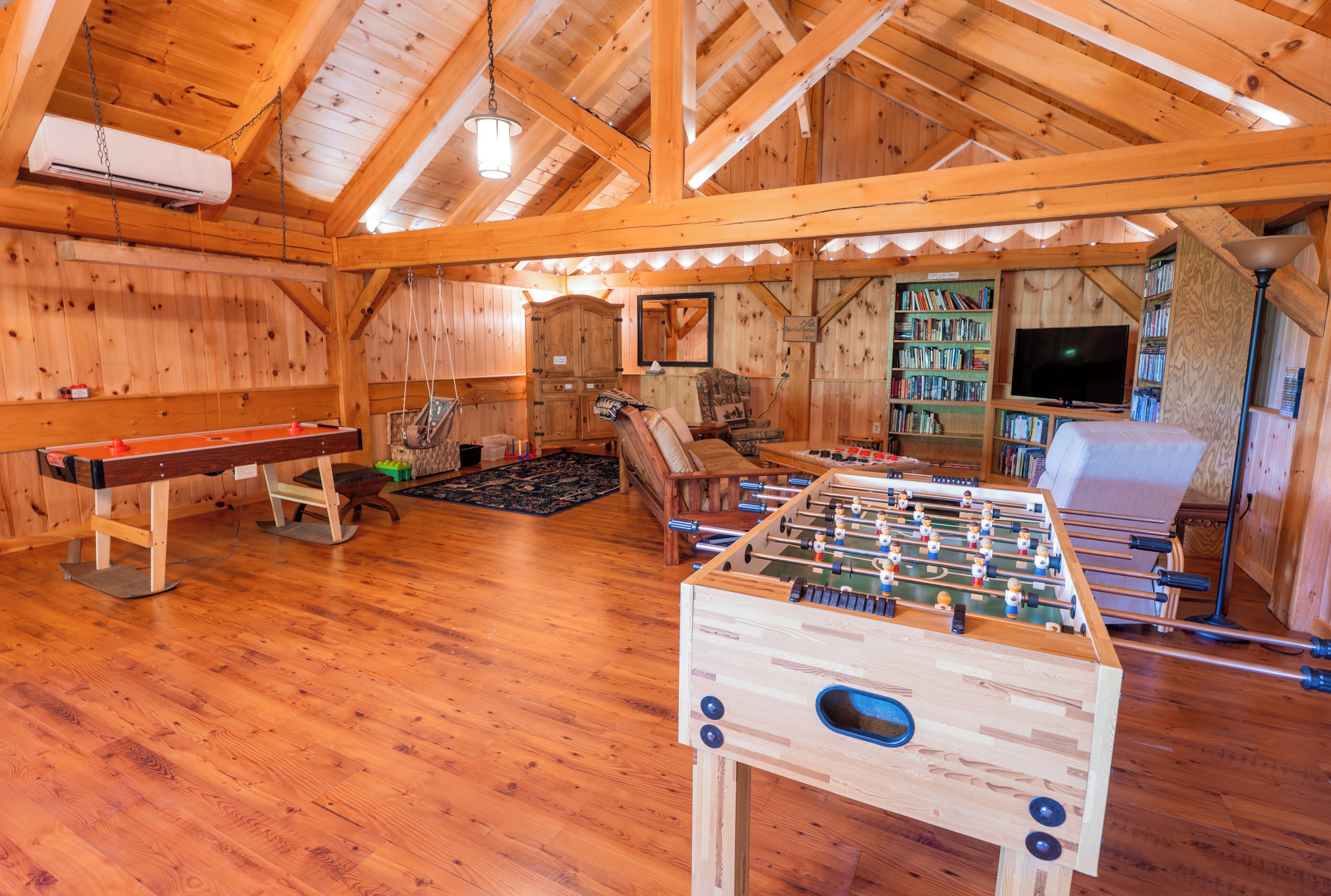 A cozy room with wooden walls, a foosball table, a sofa, a bookshelf, and a television.