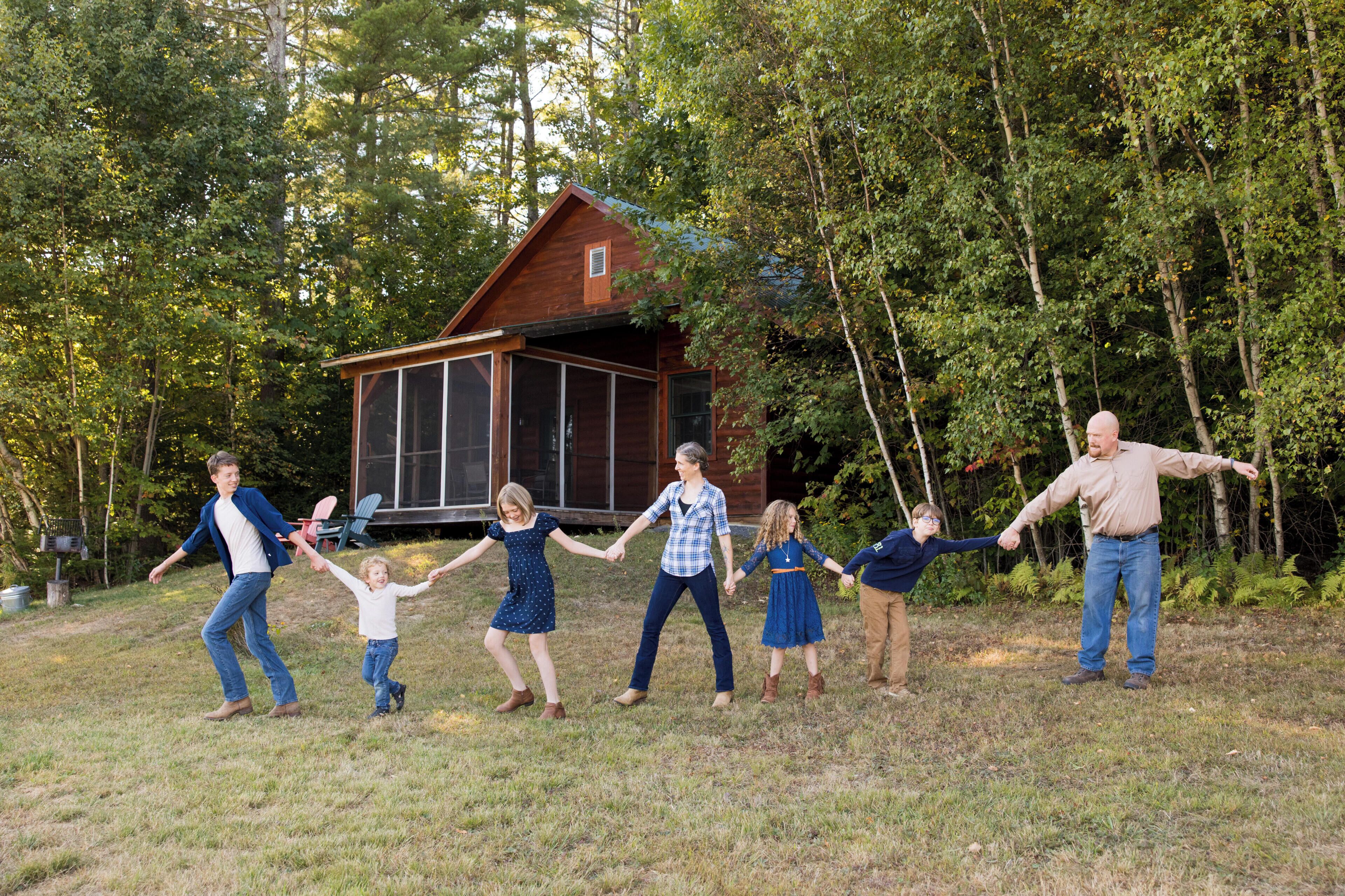 A family holding hands in a grassy area with a wooden cabin in the background.