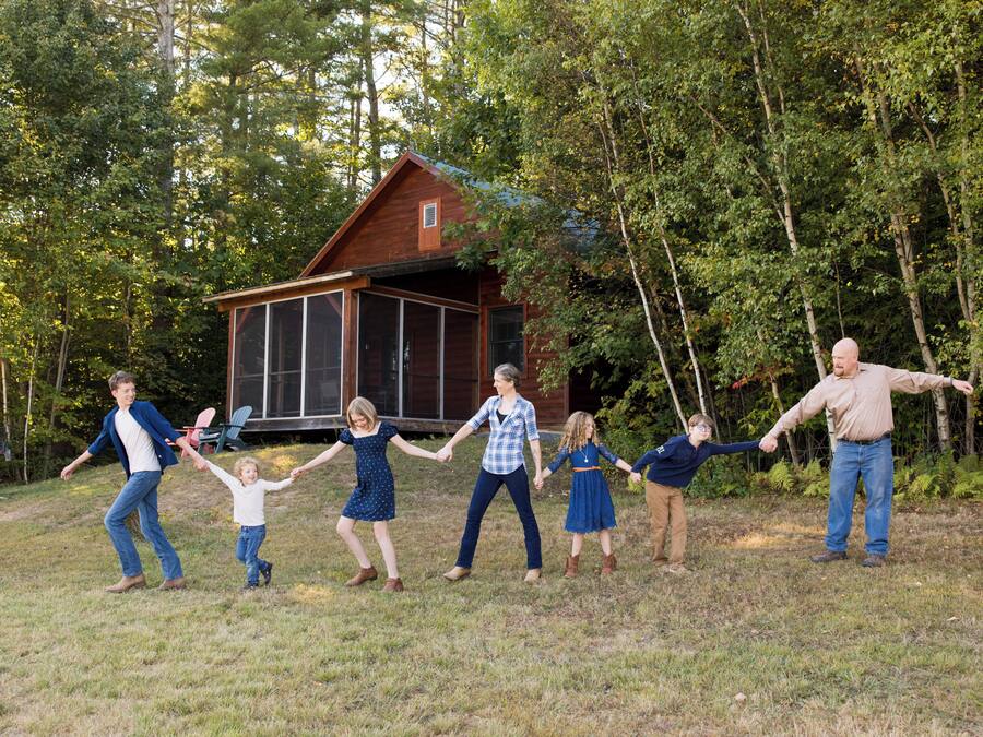 A family holding hands in a grassy area with a wooden cabin in the background.