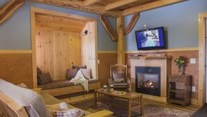 A cozy living room with a wooden ceiling, a fireplace, a television, and a comfortable seating area. - Robert Frost Mountain Cabins (Ripton)